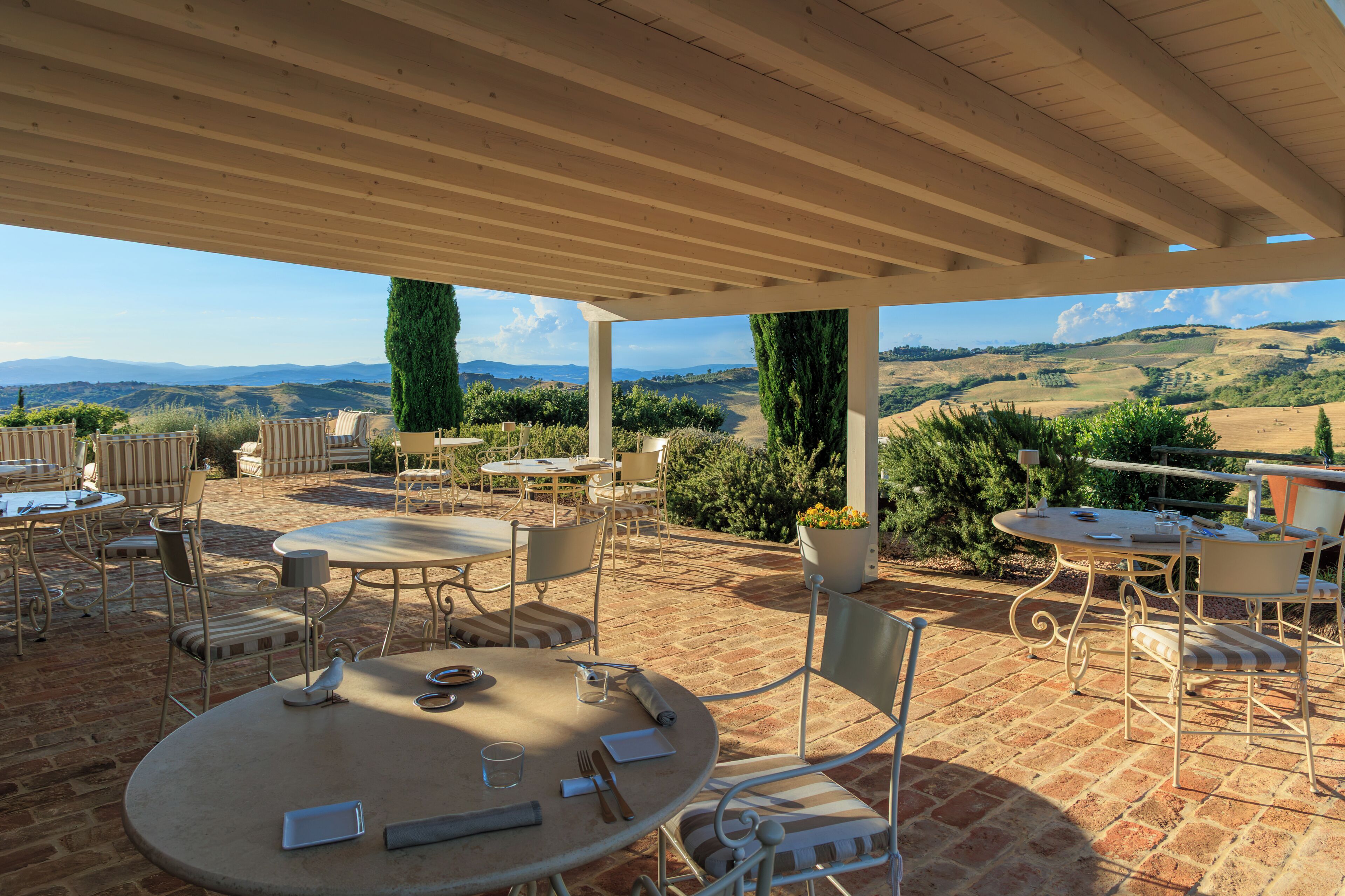 Un patio al aire libre con mesas y sillas, una pérgola y vistas a colinas ondulantes.