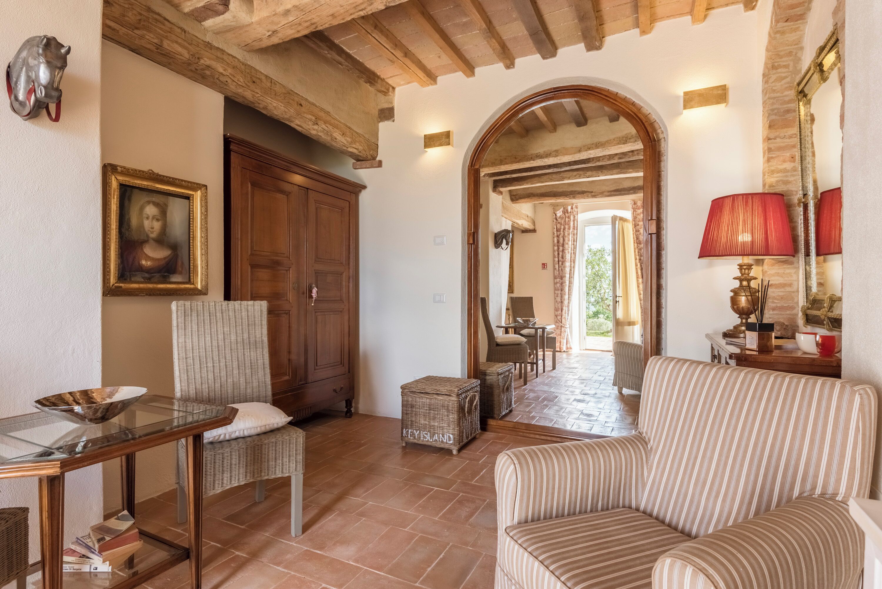 Una sala acogedora con techo de madera, un sillón de mimbre, un sofá a rayas y una mesa de vidrio.