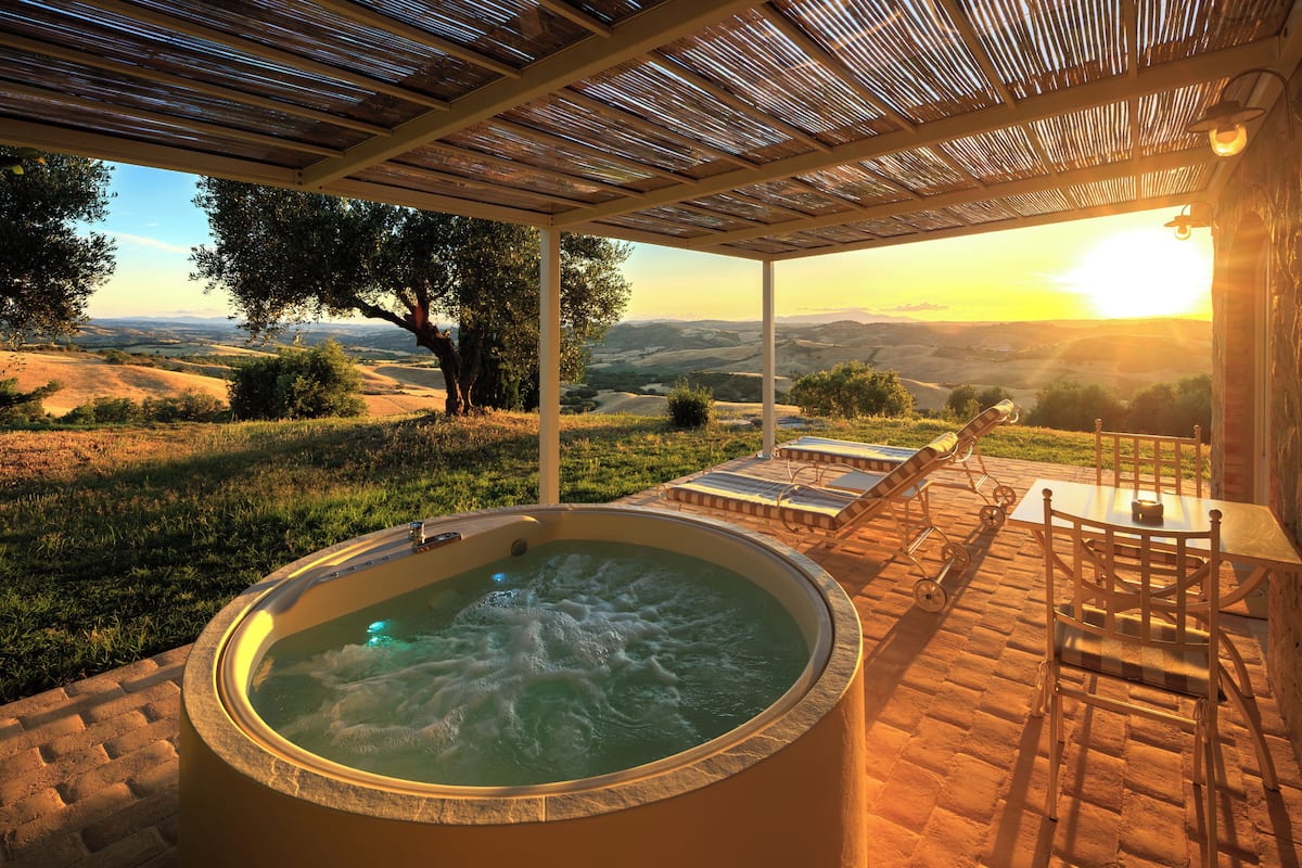 Un bain à remous avec vue sur des collines verdoyantes, un patio couvert avec des sièges et une pergola.