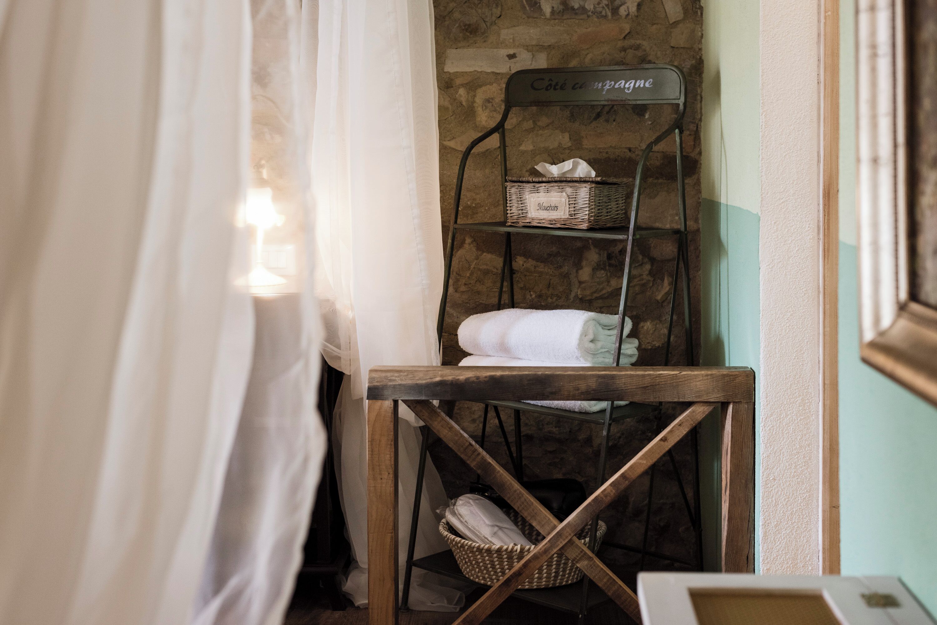 Une salle de bain avec une étagère en bois sur laquelle sont posés un panier et des serviettes, un panier en osier et un tableau encadré sur une petite table.