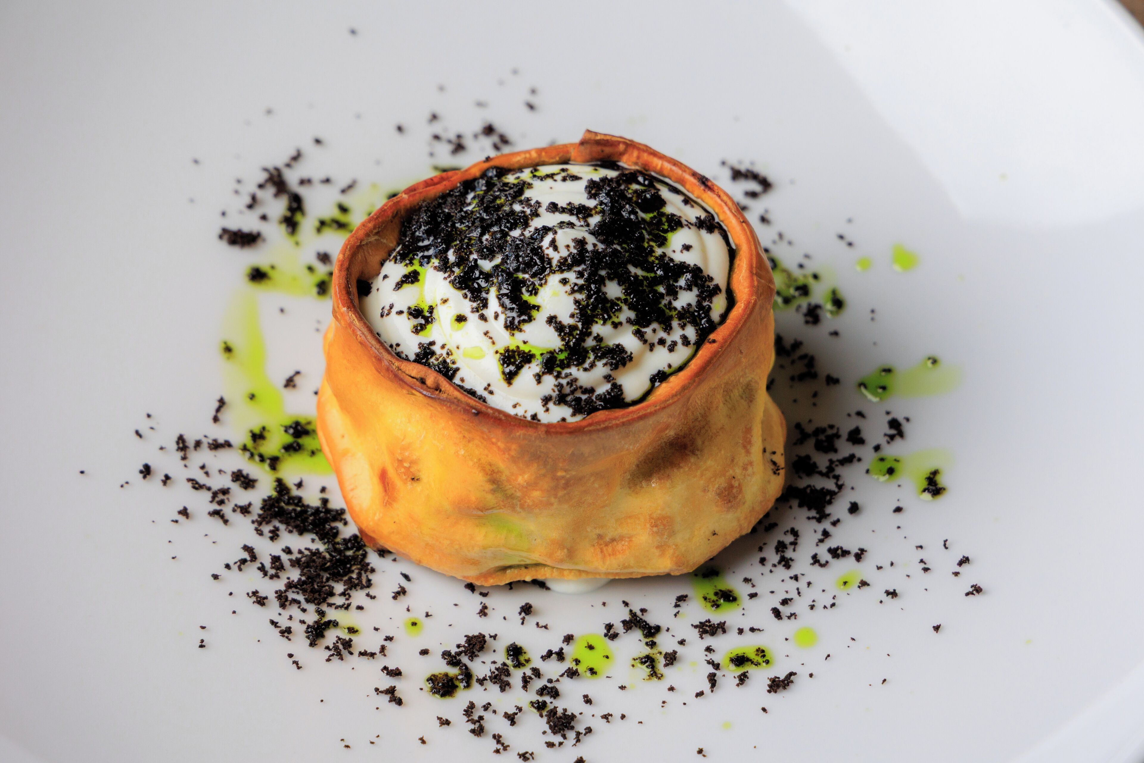 A dessert in a bowl on a plate with green and black toppings.