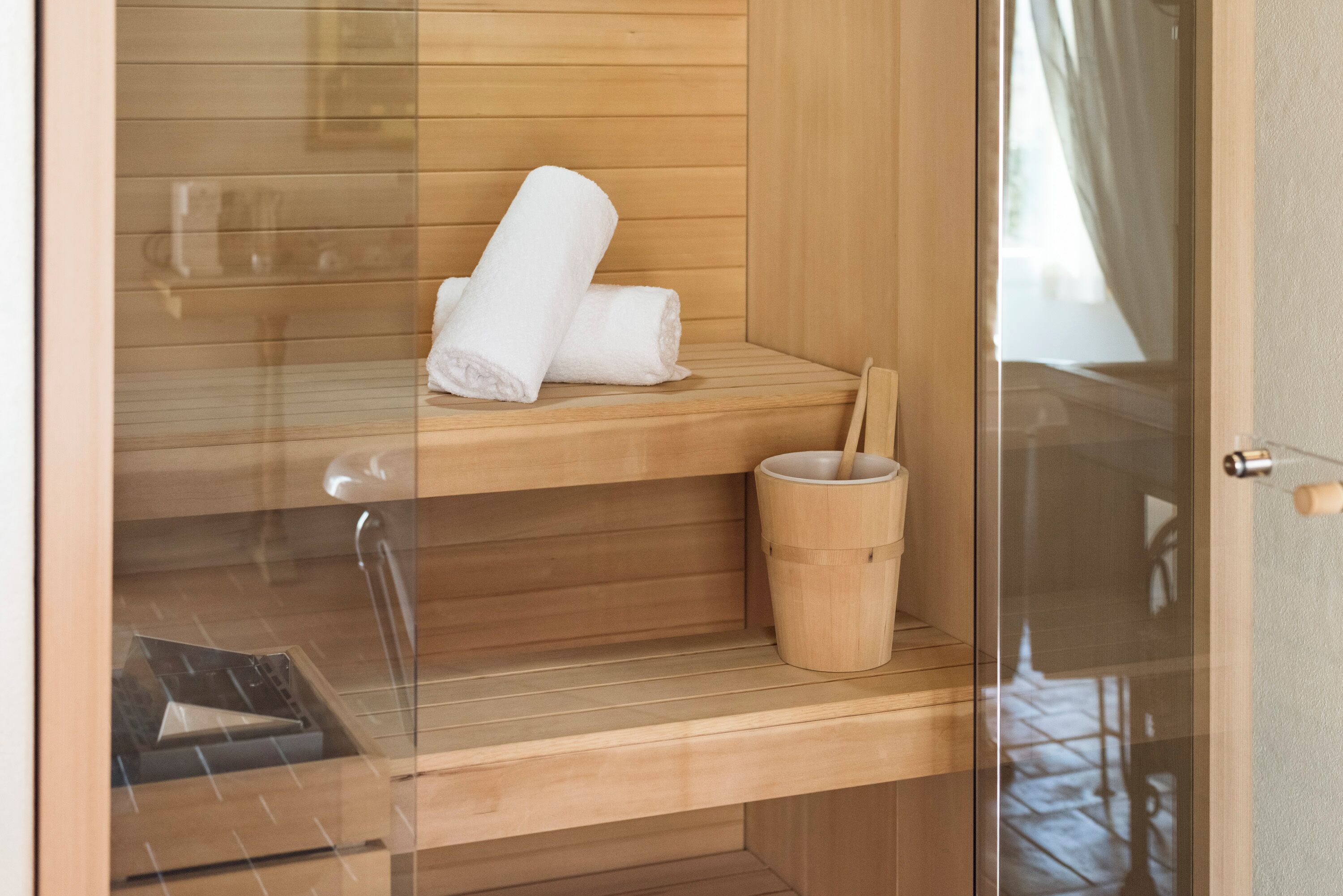 Una sauna de madera con dos estantes, uno con toallas enrolladas y el otro con un cubo de madera.