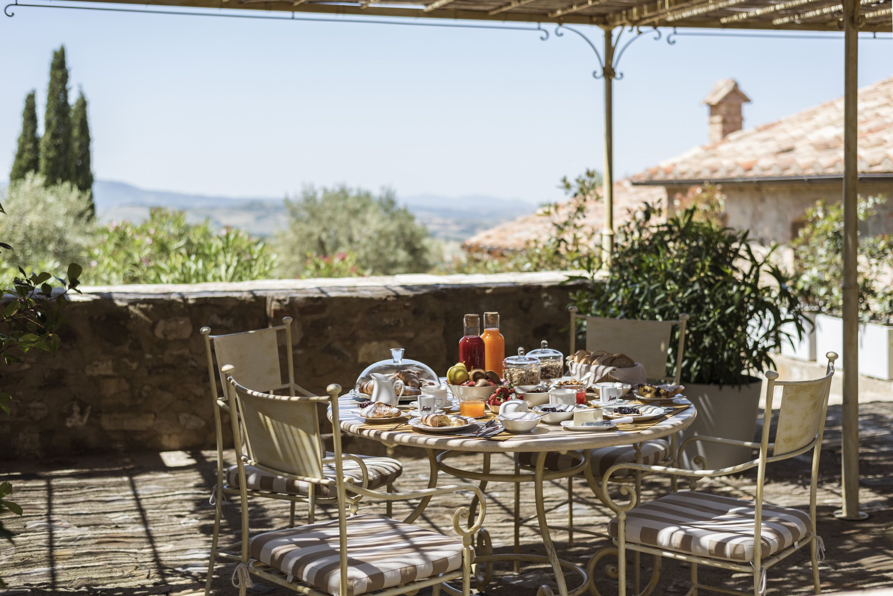 An outdoor dining area with a round table set for breakfast, surrounded by metal chairs with cushioned seats.