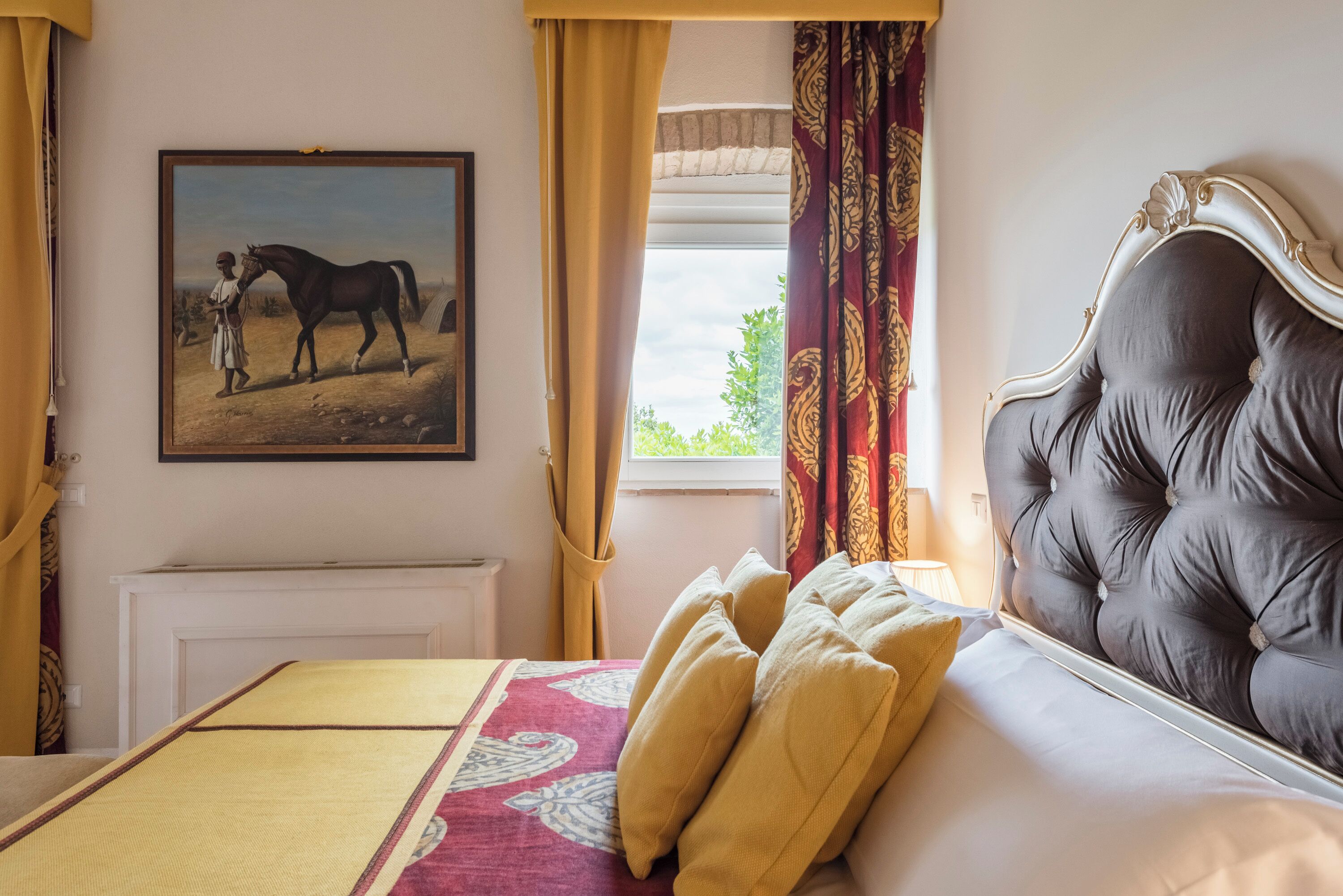 A bedroom with a large bed, a headboard, a painting of a horse, and a window with curtains.