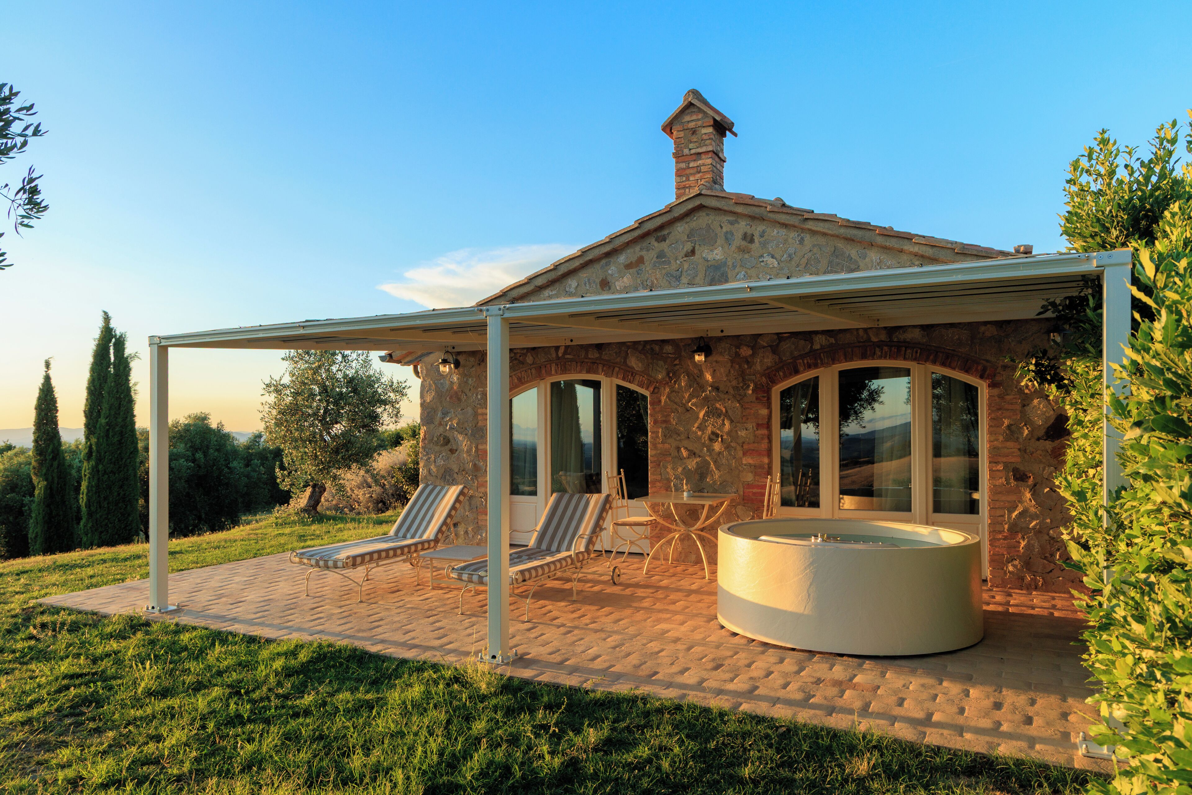 A stone house with a covered patio, lounge chairs, and a hot tub.
