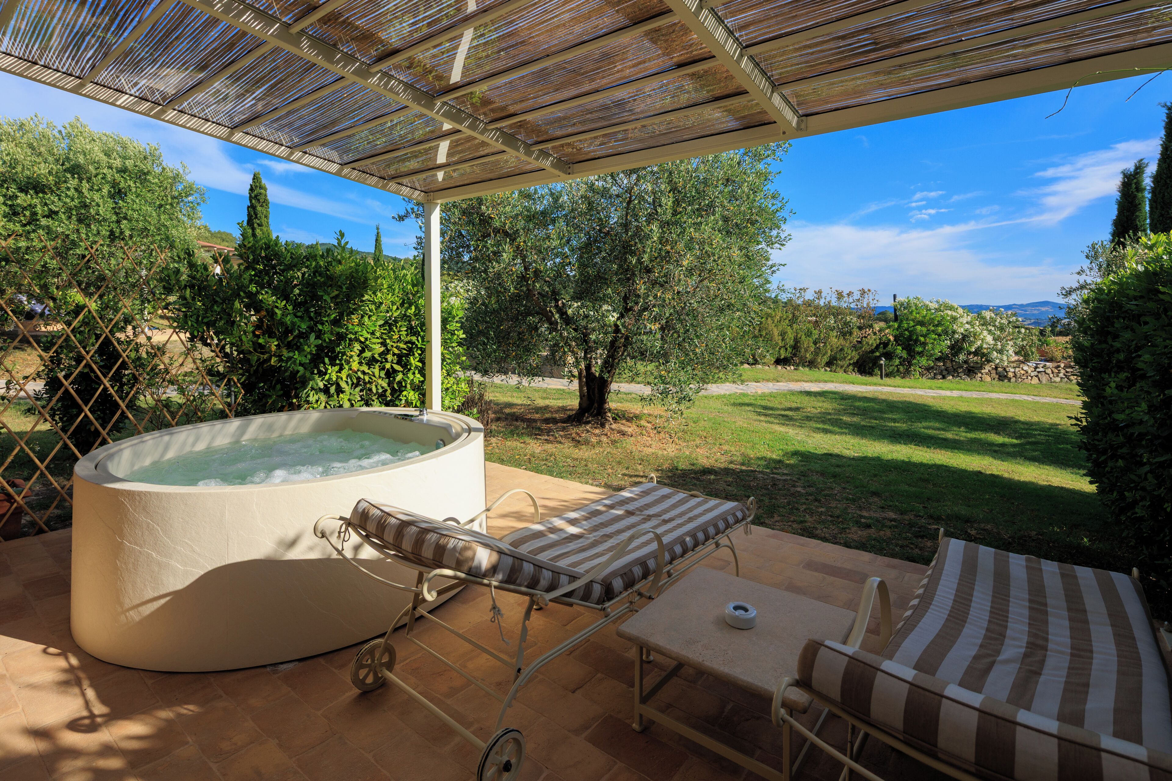 A hot tub, lounge chairs, and a covered patio area with a view of the landscape.