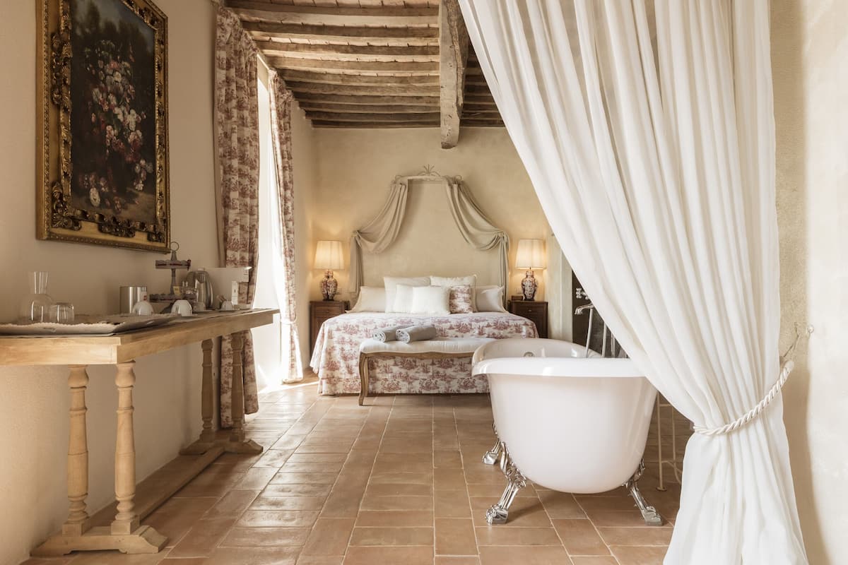 Une chambre à coucher avec un grand lit, une baignoire, une table en bois et un tableau accroché au mur.