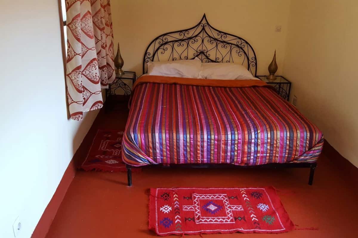 A bed with a striped bedspread, a red rug, and a decorative pillow.