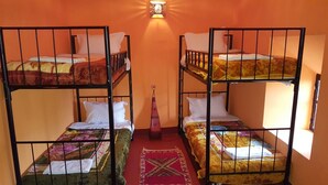 Quarto tipo dormitório com beliches, tapete vermelho e luminária fixada na parede.