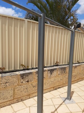 A metal railing with a beige wall and stone base in the background.