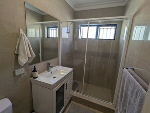 A bathroom with a glass-enclosed shower, a white sink with a soap dispenser, and a towel hanging on the wall.