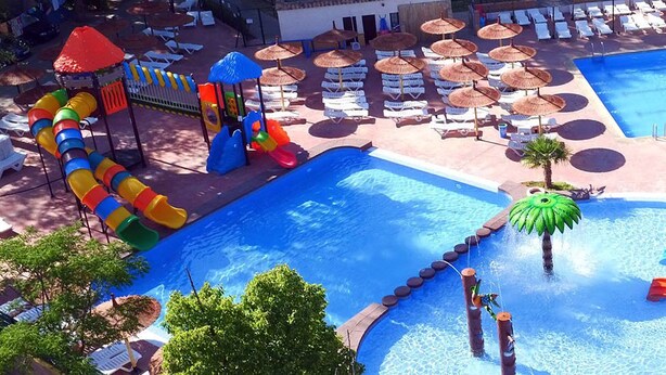 Ein Poolbereich mit mehreren Wasserrutschen, Liegestühlen und Sonnenschirmen.