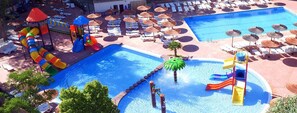 Un área de piscina con varias toboganes, sillas de descanso y sombrillas.