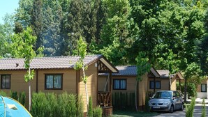 Eine Reihe aus Holzbungalows mit einem geparkten Auto davor, umgeben von Bäumen und einem Zelt.
