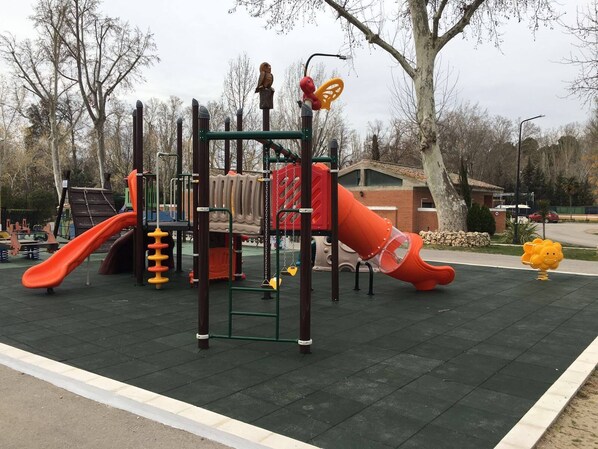 Un parque infantil con tobogán, estructuras para escalar y columpios.
