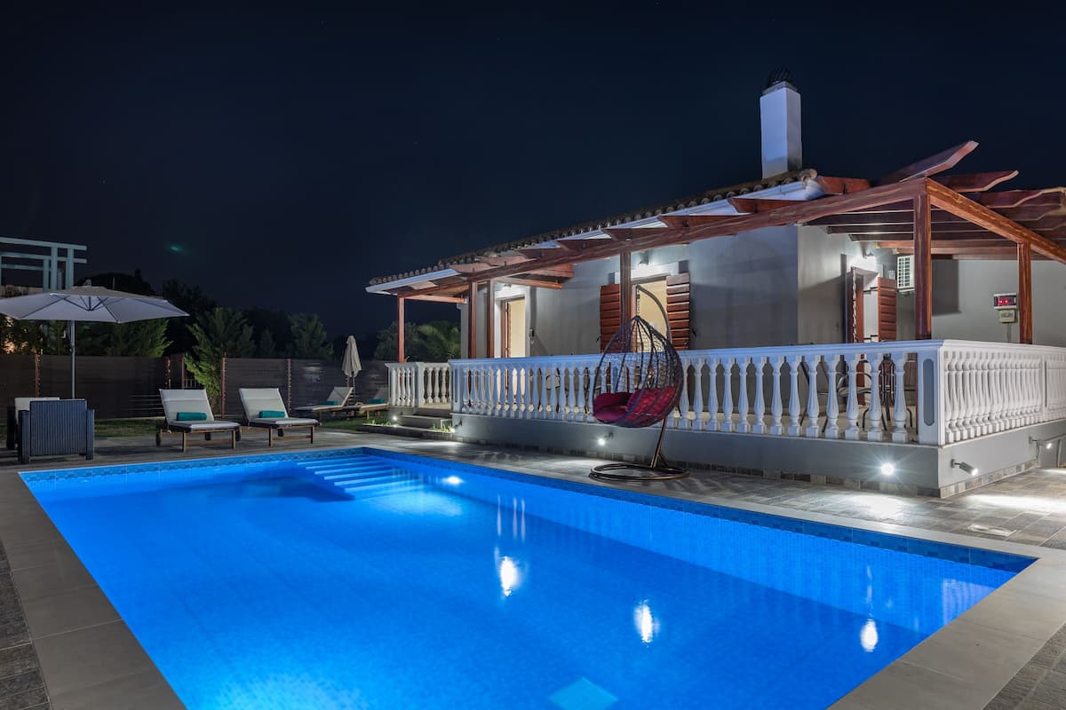A swimming pool with lounge chairs and a hanging chair, surrounded by a covered patio area with a railing.