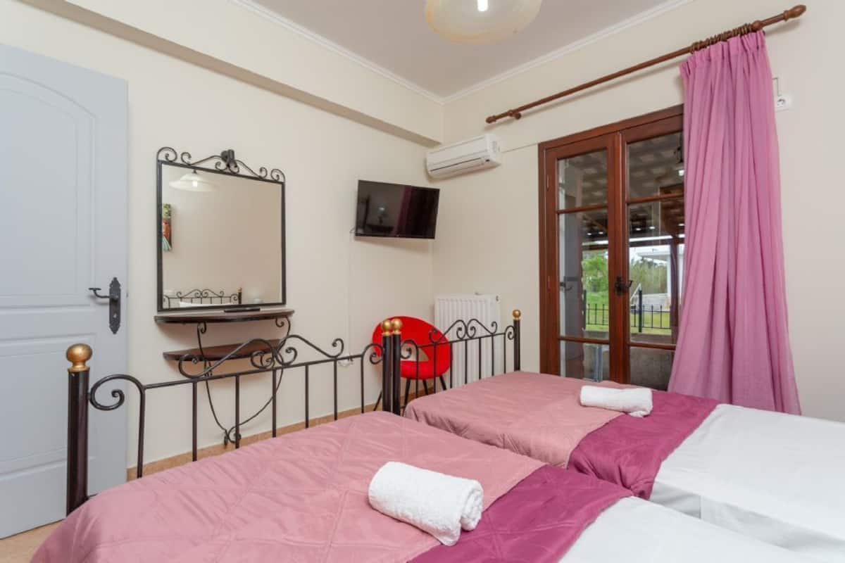 A bedroom with two beds, a TV, a red chair, and a window with a view.