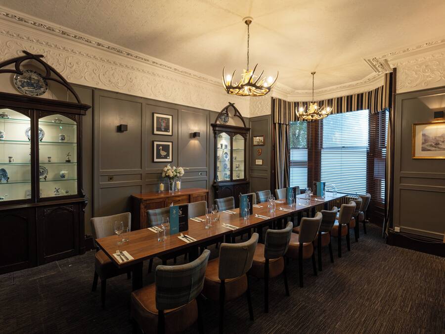 Uma sala de jantar formal com uma mesa comprida posta para refeição, rodeada por cadeiras, com um candelabro e iluminação na parede.