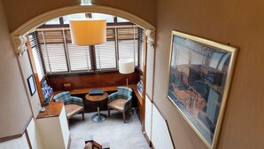 A cozy room with a wooden bench, two chairs, a small table, and a lamp. A framed picture of Edinburgh is on the wall.