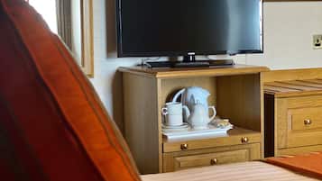 A hotel room with a bed, a television on a wooden stand, a small table with a kettle and cups, and a poster on the wall.