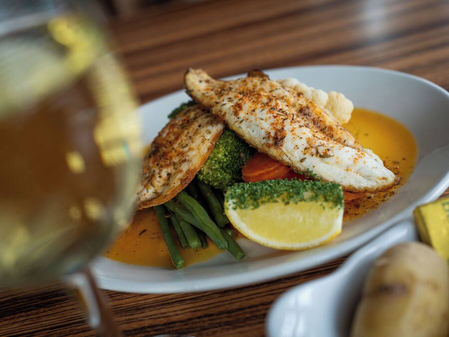 A plate of food with fish, vegetables, and a lemon wedge.