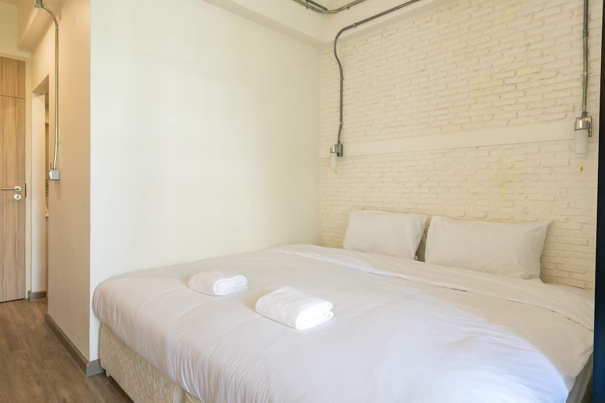 Hotellihuone, jossa on tiiliseinä, valkoisilla lakanoiden peitetty sänky ja ovi vasemmalla puolella.