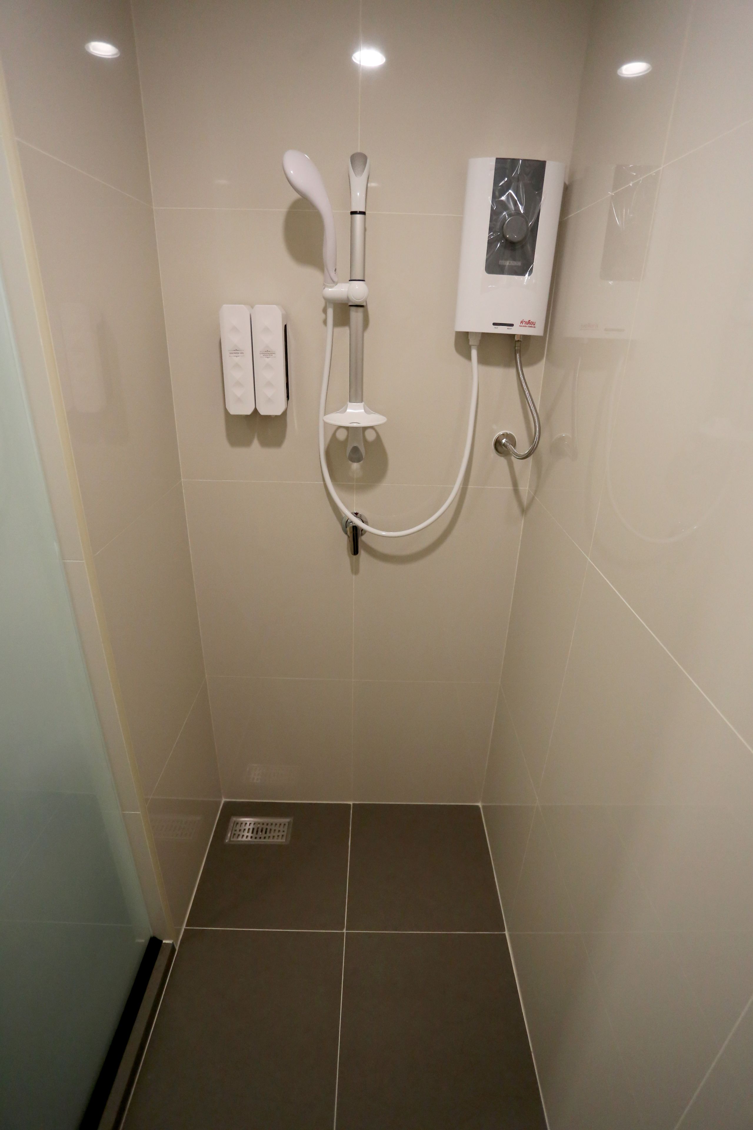 A shower with a handheld showerhead, a wall-mounted control panel, and two towel dispensers.