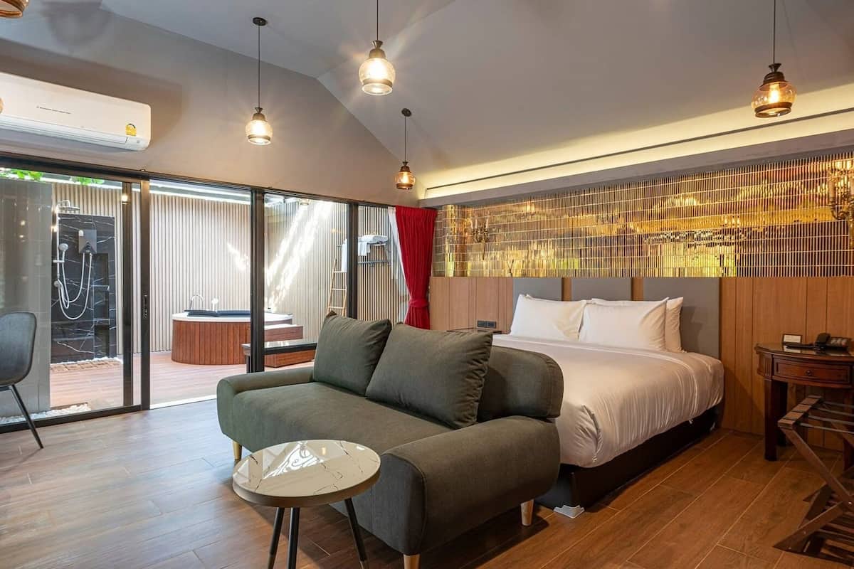 Moderni hotellihuone, jossa on sänky, sohva ja pieni pöytä. Huoneesta on liukuovet, jotka johtavat ulkotilaan, jossa on poreallas.