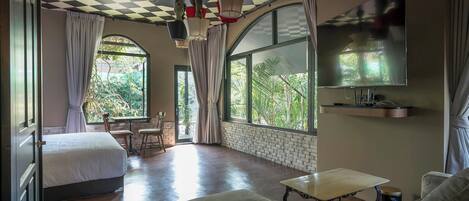 Una habitación amplia con techo a cuadros, ventanas grandes, una cama, un sofá y una mesa.