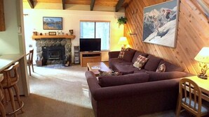 Ein gemütliches Wohnzimmer mit Kamin aus Stein, einem Fernseher und einer Couch mit Kissen.