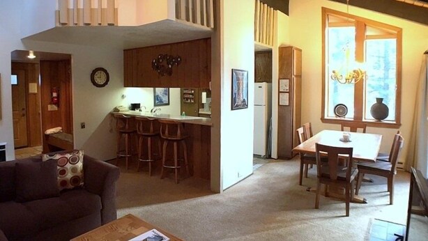 Ein großzügiger Wohnbereich mit einer Couch, einem Couchtisch, einem Esstisch mit Stühlen, einer Küche mit Bar und einem großen Fenster für natürliches Licht.
