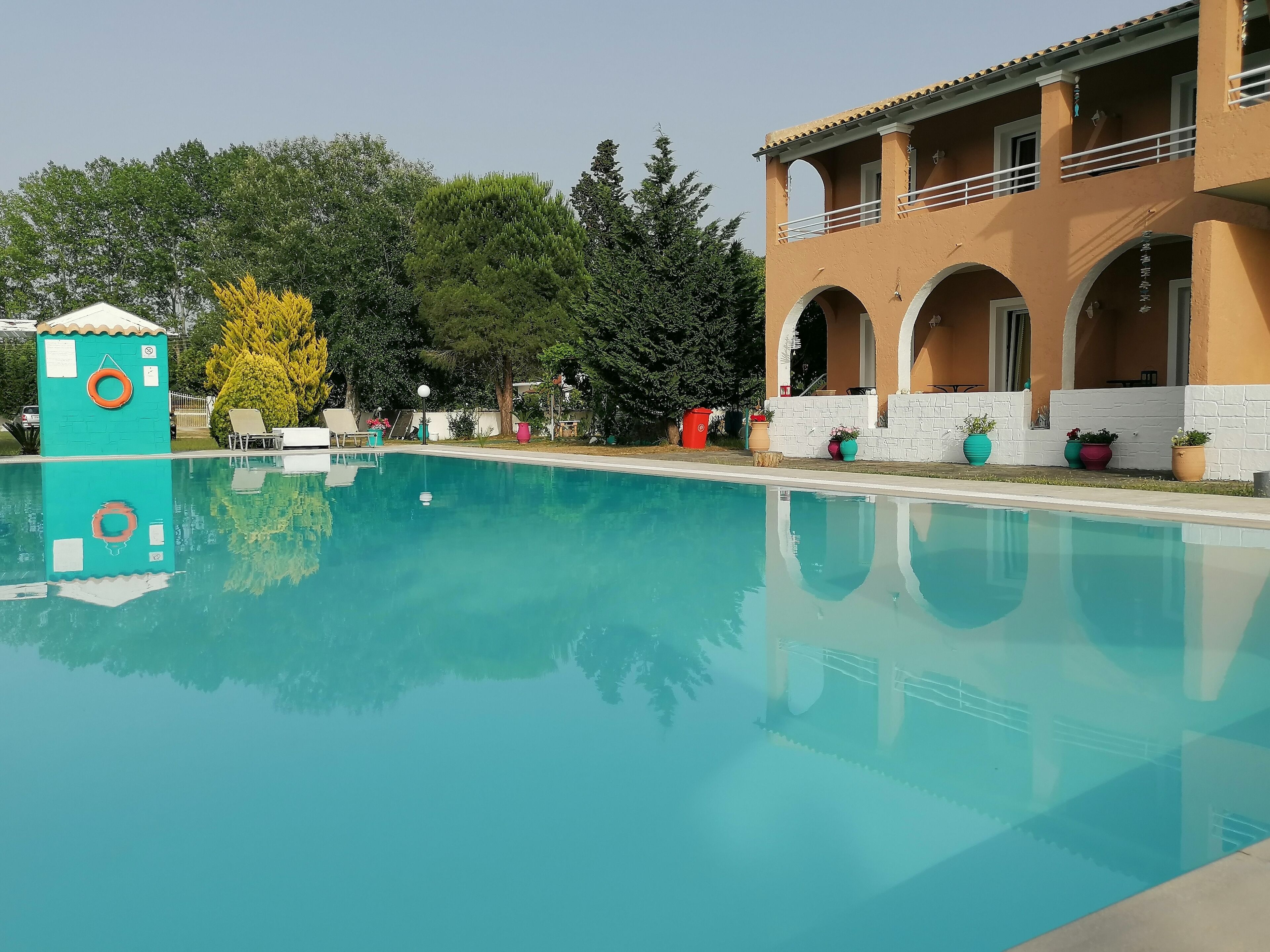 Une piscine à l’eau d’un bleu limpide, entourée d’un bâtiment doté de fenêtres en arc de cercle et d’un balcon.