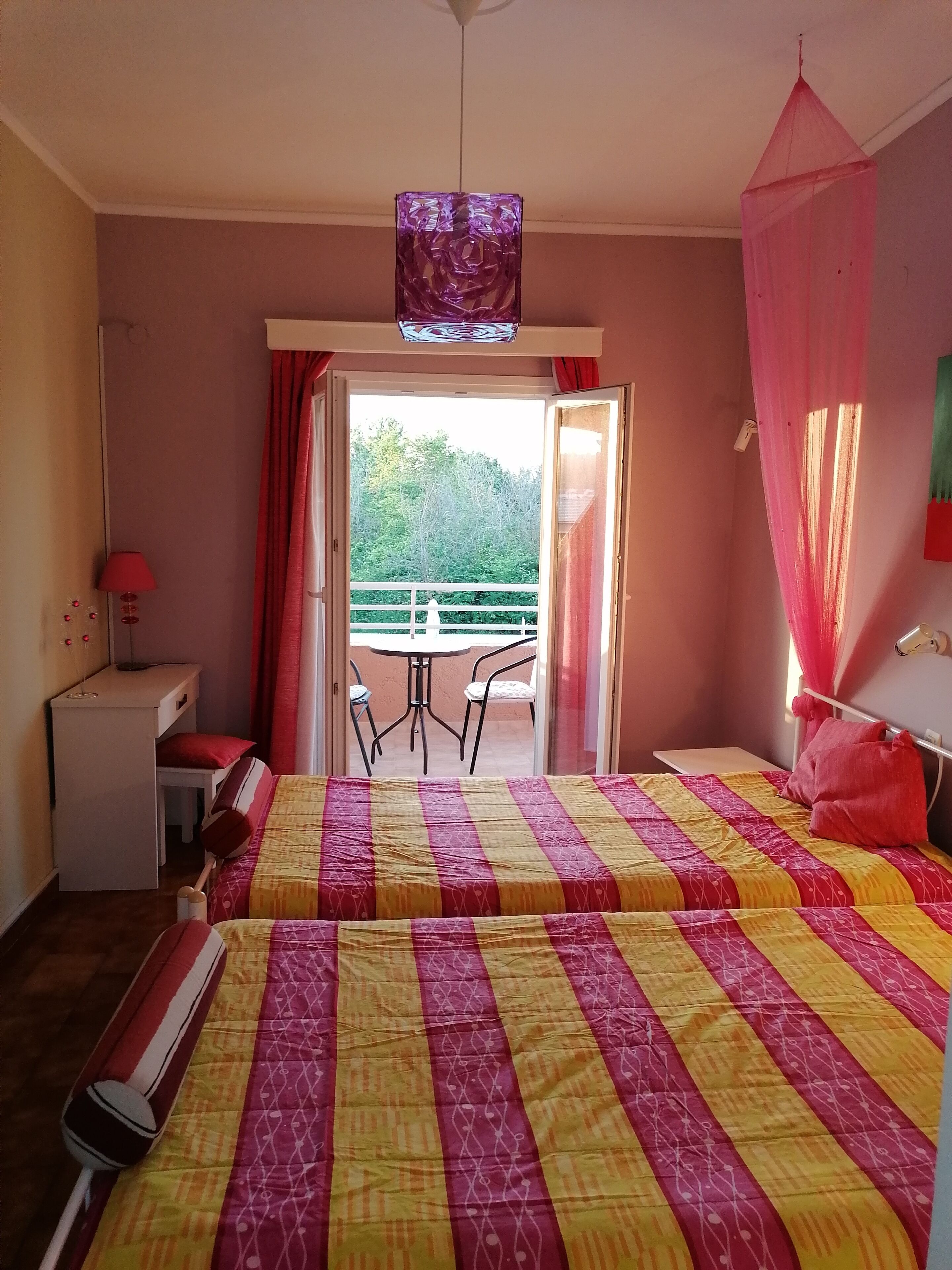 Une chambre d’hôtel avec deux lits, un bureau, une chaise et un balcon équipé d’une table et de chaises.
