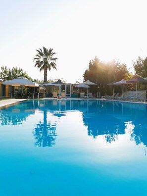 A clear blue pool with lounge chairs and umbrellas, surrounded by trees and a palm tree. - Sausan Hotel (Corfu)