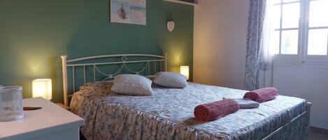 Cama bem arrumada com roupa de cama floral, mesa de cabeceira com abajur e unidade de ar condicionado na parede.