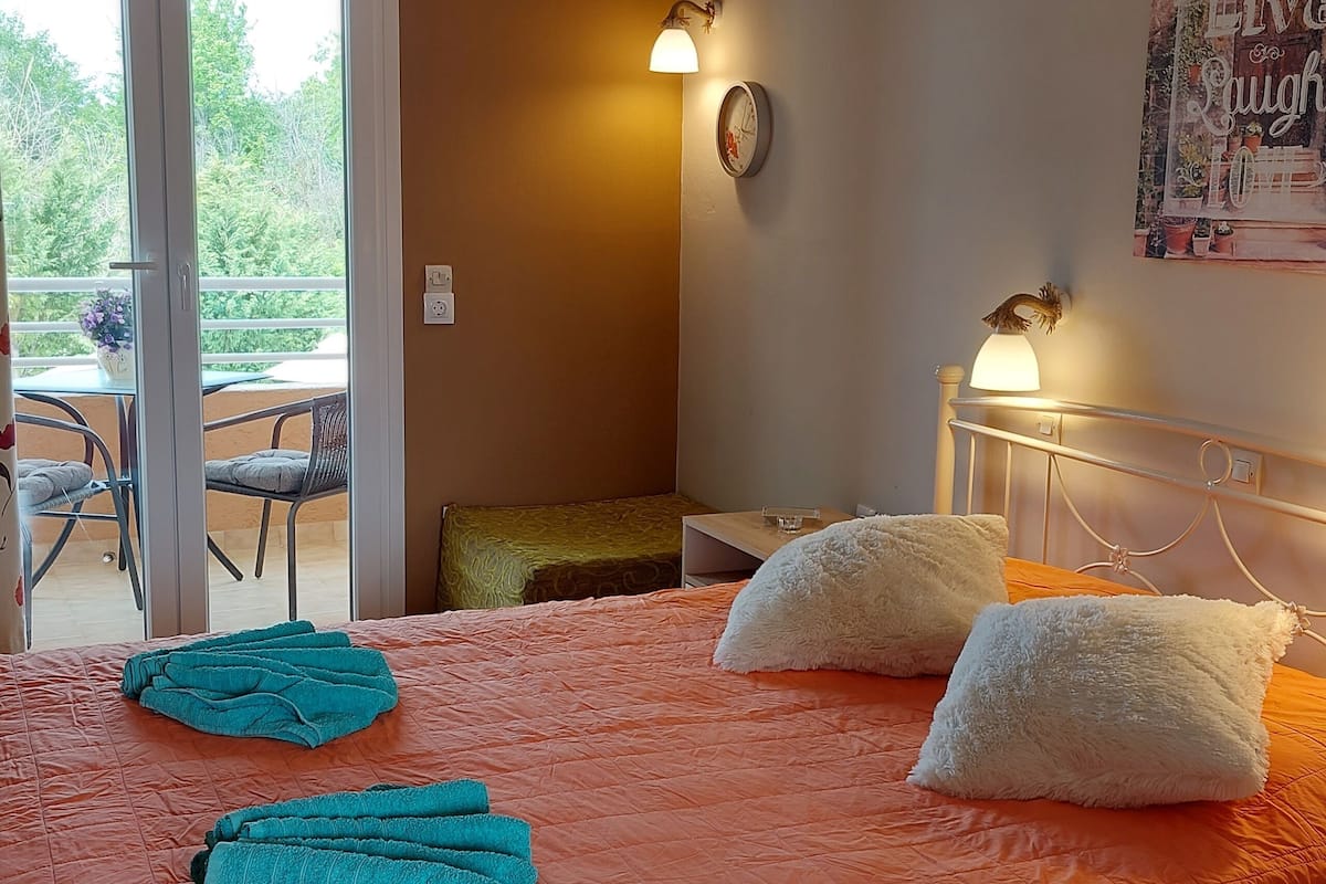 A bedroom with an orange bedspread, two white pillows, a dreamcatcher, a wall clock, and a poster.