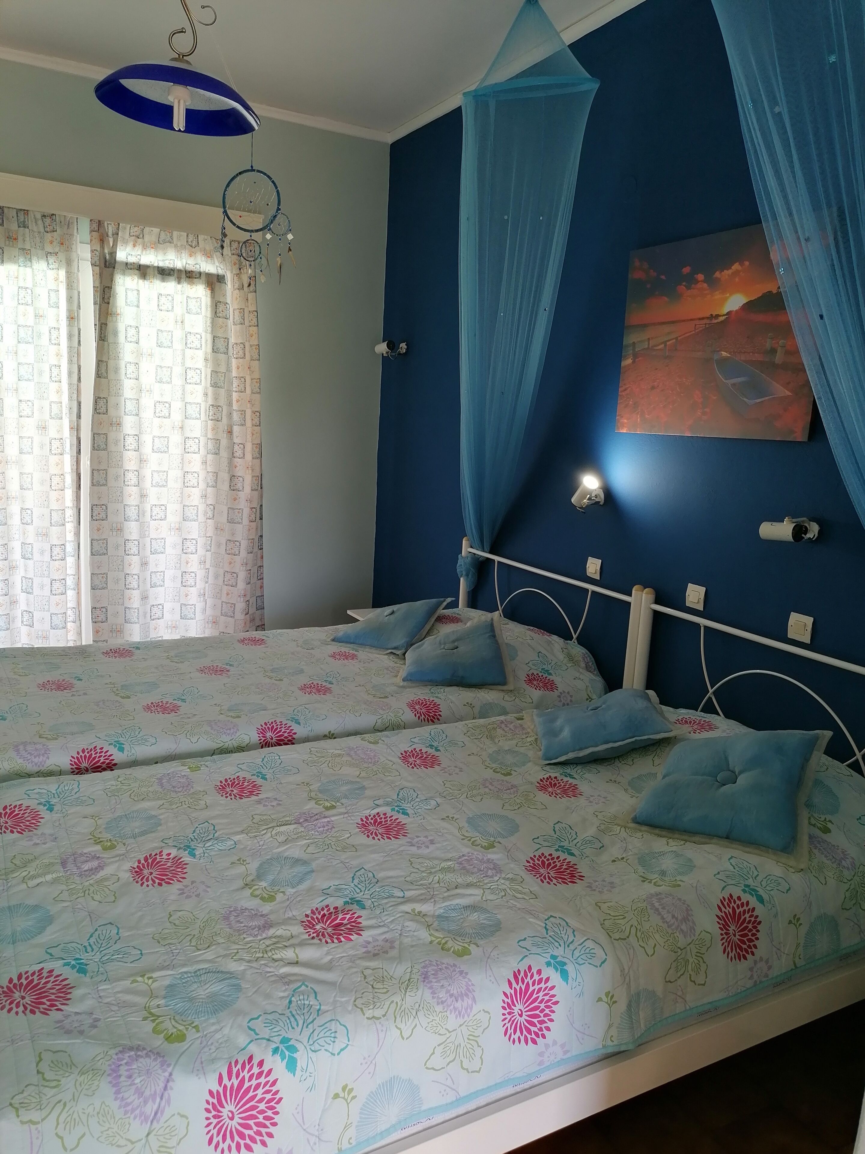 A bedroom with a bed, curtains, a dreamcatcher, a painting, and a ceiling light.