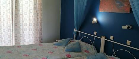 A bedroom with a bed, curtains, a dreamcatcher, a painting, and a ceiling light.