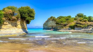 A beach with clear turquoise waters, rocky cliffs, and lush greenery. - Sausan Hotel (Corfu)