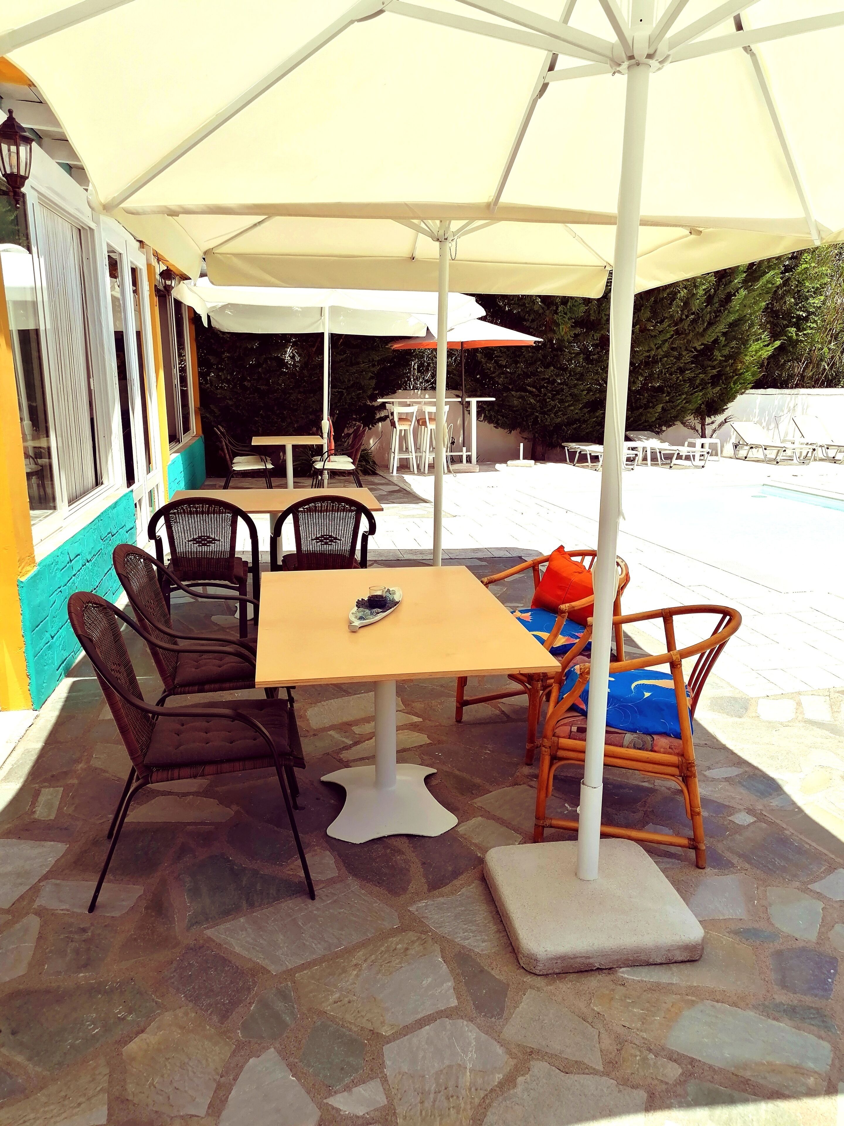 Un patio al aire libre con mesa, sillas, piscina y sombrillas.