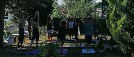 Um grupo de pessoas praticando yoga ao ar livre, com árvores e uma área gramada.