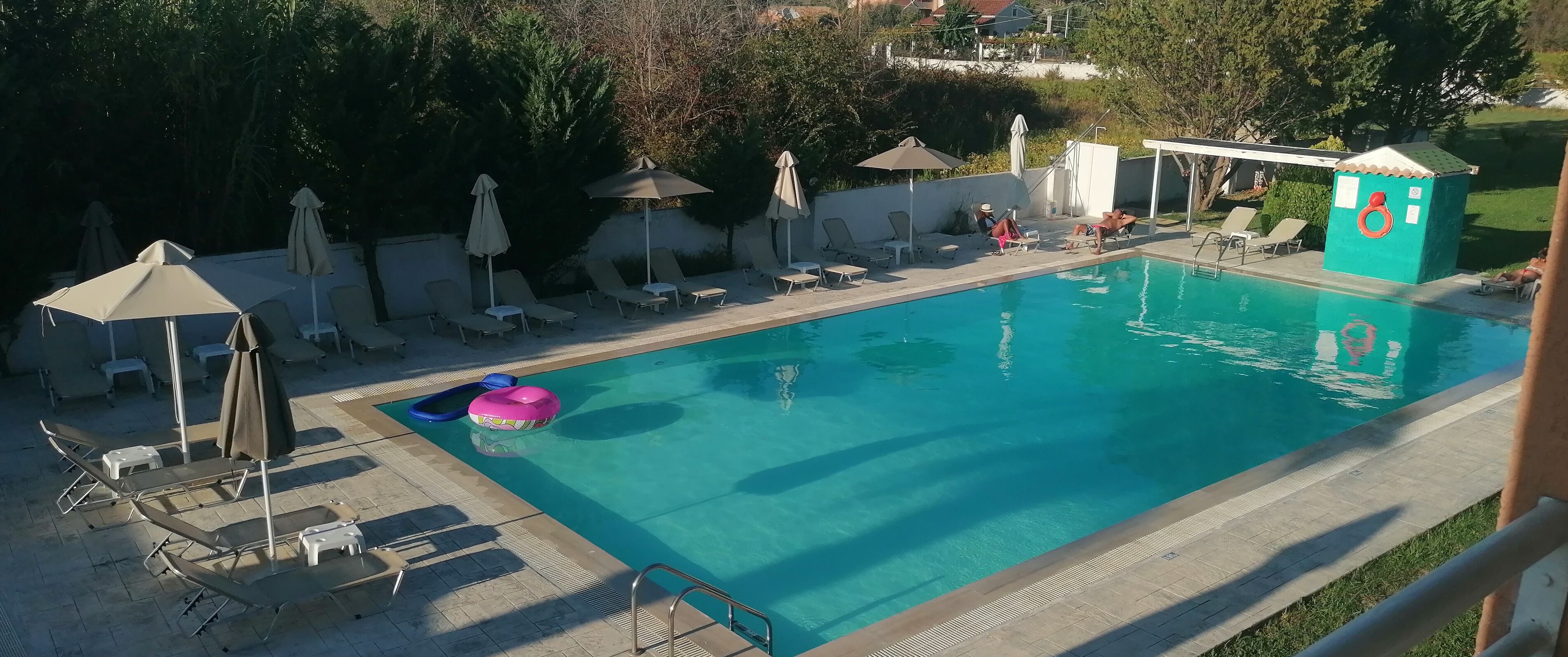 A swimming pool with lounge chairs and umbrellas, surrounded by trees and a covered area.