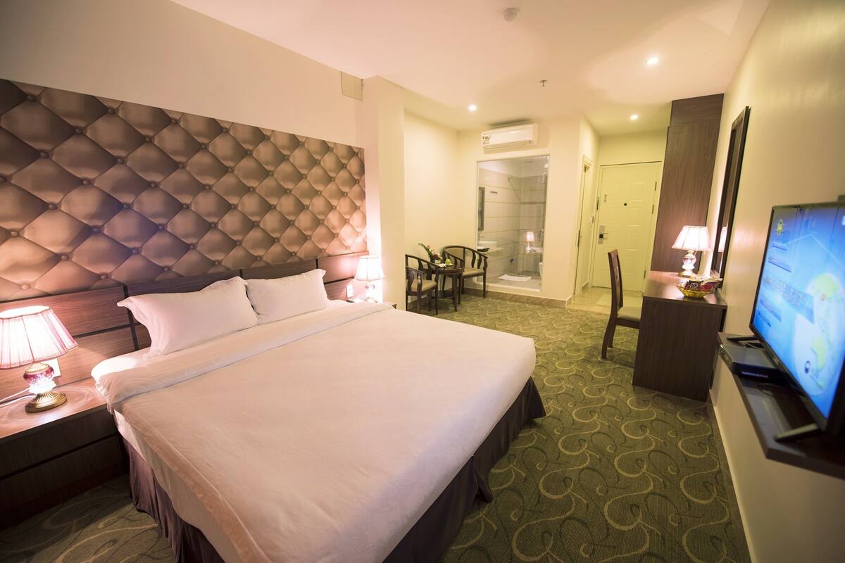 A hotel room with a large bed, a television, a desk with a lamp, and a chair.