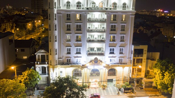 Um hotel grande e com vários andares, com uma entrada imponente, várias varandas e uma torre com relógio.