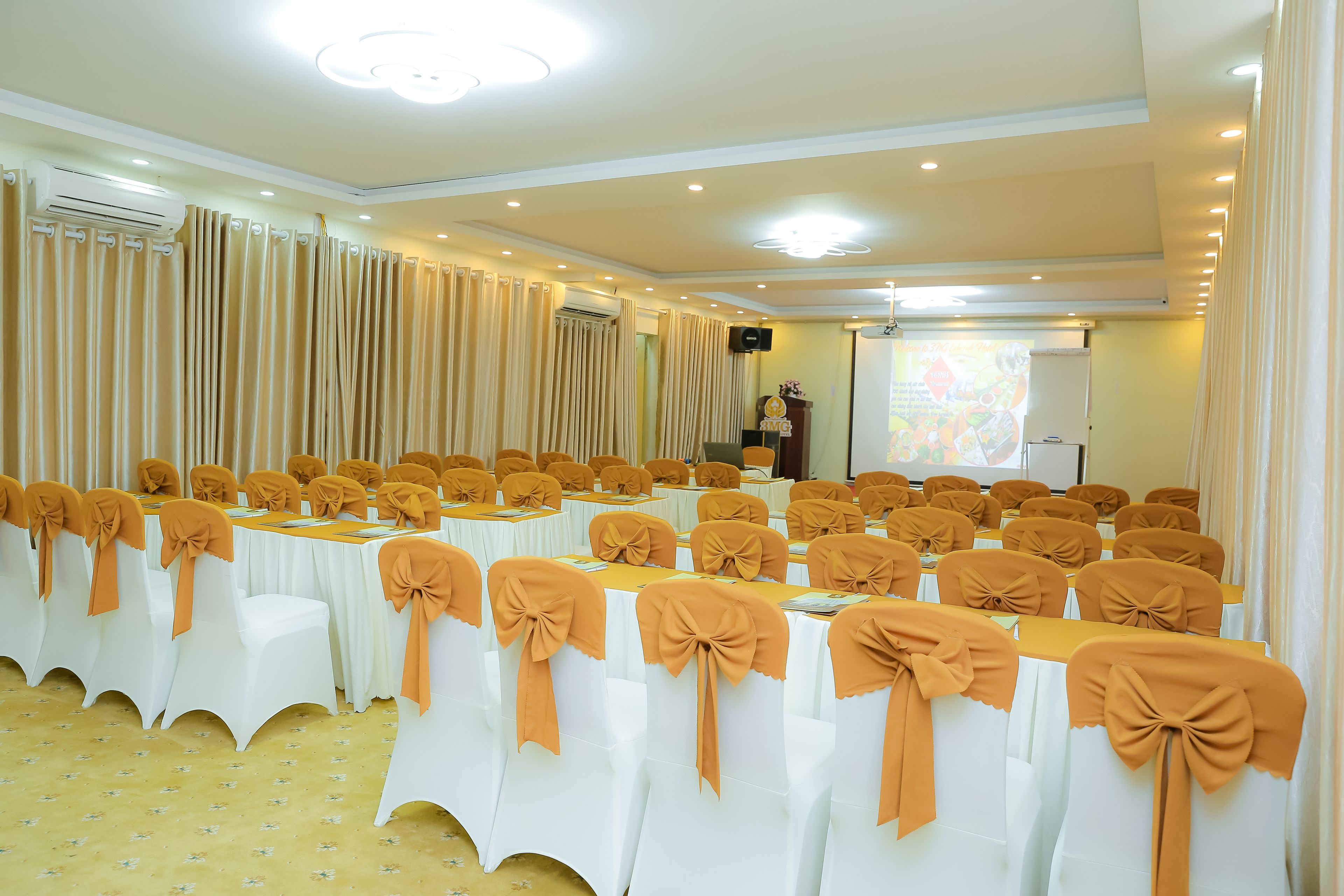 A conference room with rows of white tables, each with a brown chair and a matching brown table runner.