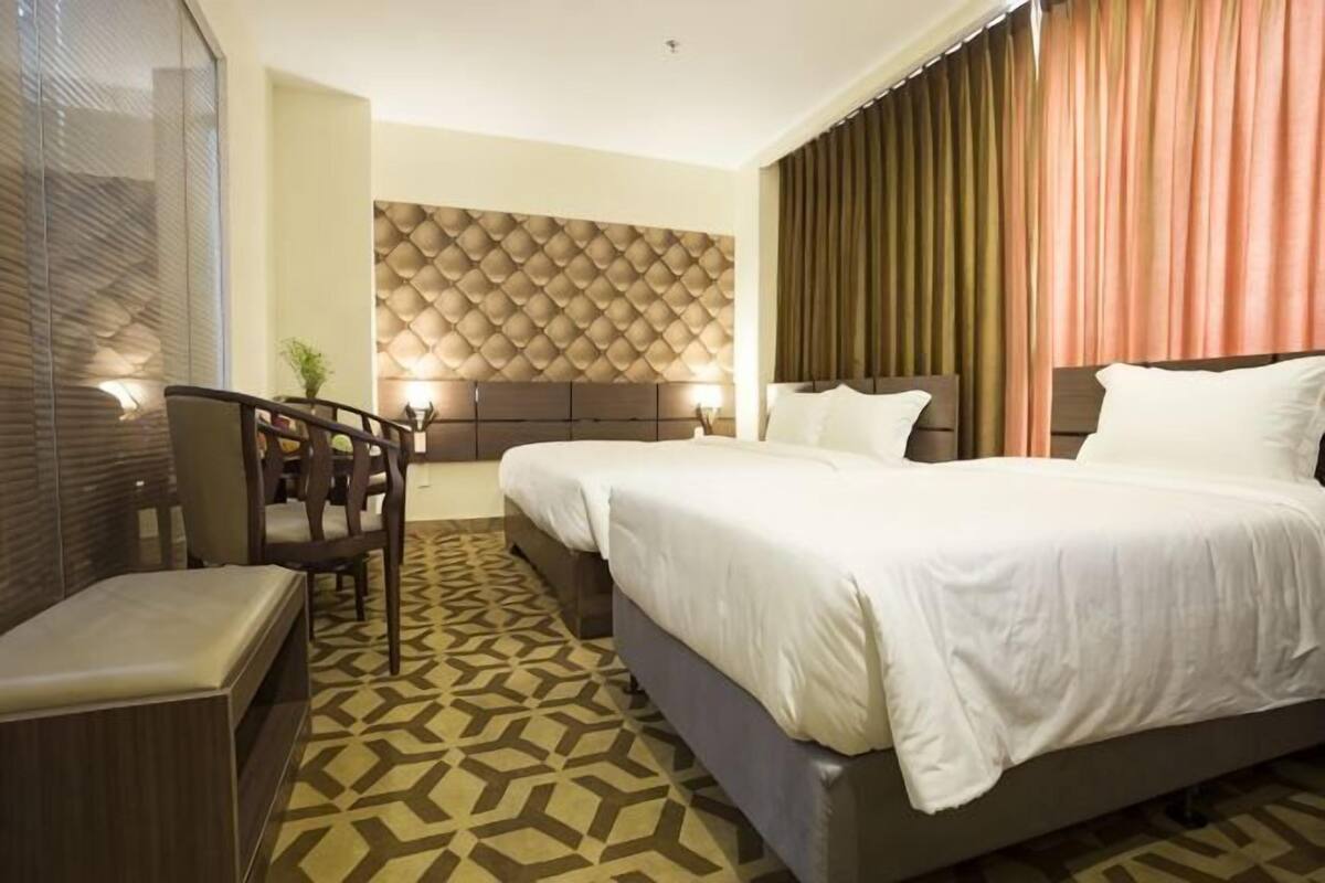 A hotel room with two beds, a seating area, a patterned floor, and a textured wall.