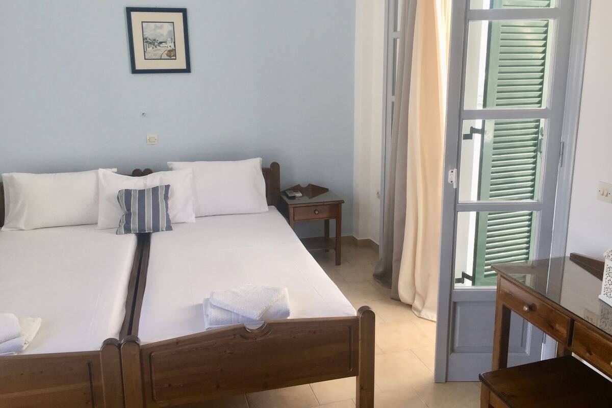 A bedroom with a bed, pillows, a bedside table, a nightstand, a framed picture on the wall, and a window with curtains.