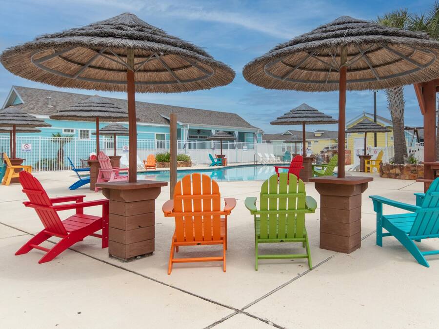 A poolside area with colorful Adirondack chairs and thatched umbrellas.