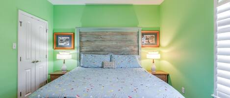 A bedroom with a bed, two nightstands, a door, and two framed pictures on the wall.