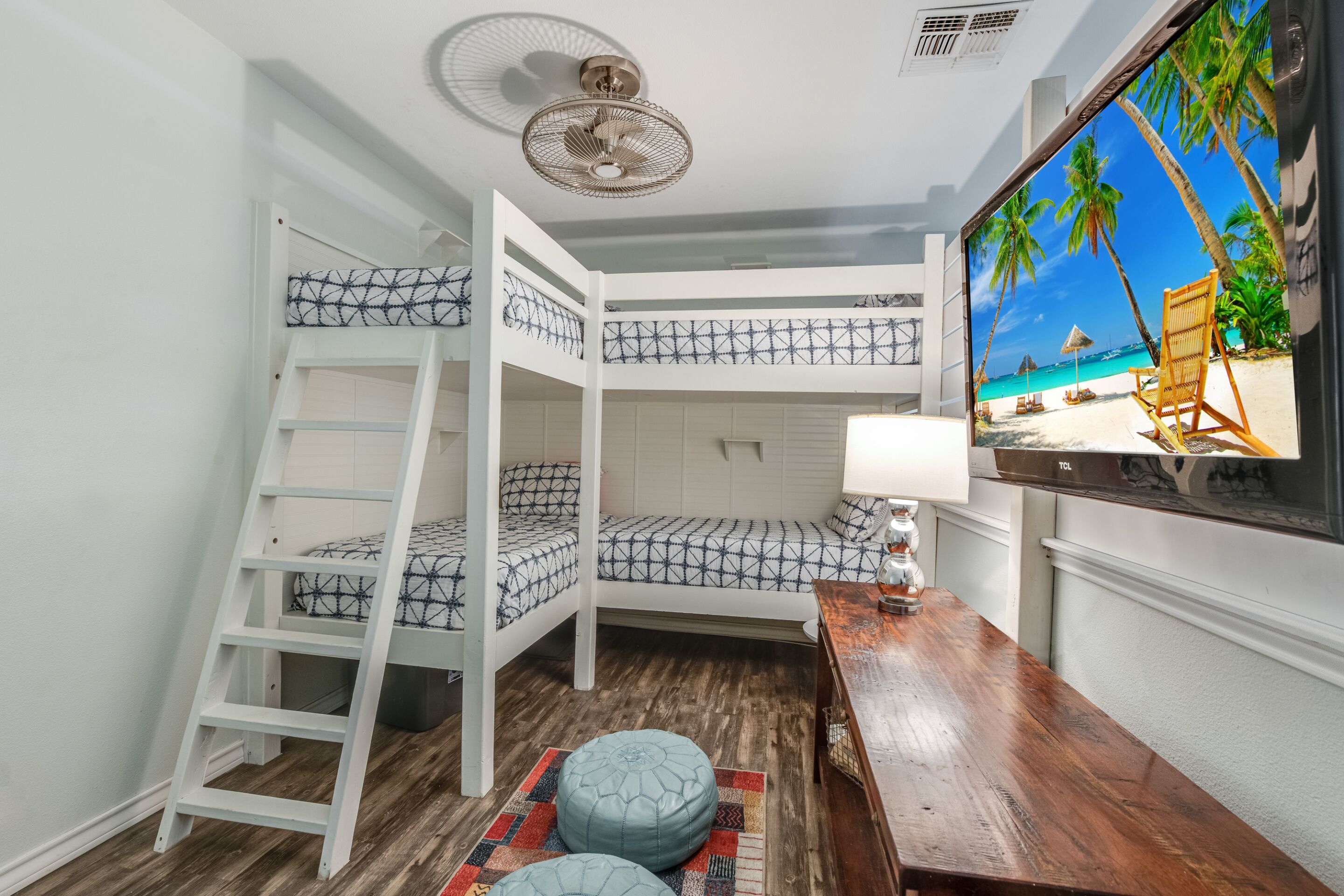 Habitación con literas, una televisión mostrando una playa, un escritorio de madera y una escalera.